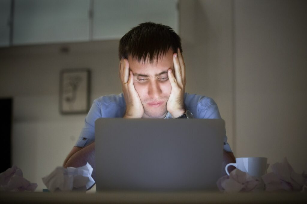 Man experiencing stress or burnout while working on his laptop, highlighting the impact of work-related stress on mental health in men.