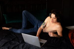 Man relaxing on the bed while using a laptop, reflecting the importance of digital well-being and self-care for men's mental health.